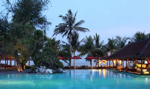 Ein ruhiger Poolbereich in Bali, umgeben von Palmen und einem traditionellen balinesischen Pavillon im Abendlicht.
