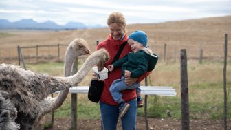 Fröhliches Baby auf dem Arm der Mutter beim Füttern von Straußen auf der Skeiding Guest Farm – Garden Route Familienreise