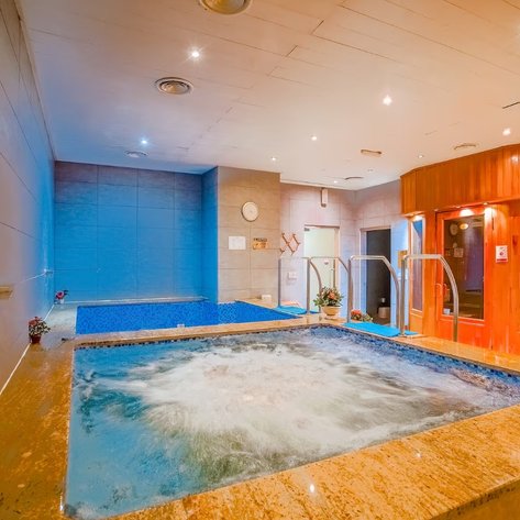 Ein entspannender Wellnessbereich mit einem sprudelnden Whirlpool und einem blauen Pool, umgeben von modernen Fliesen.