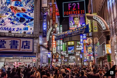 Bunte Neonlichter erhellen eine belebte Straße in Tokio, wo Menschen zwischen Geschäften und Werbetafeln schlendern.