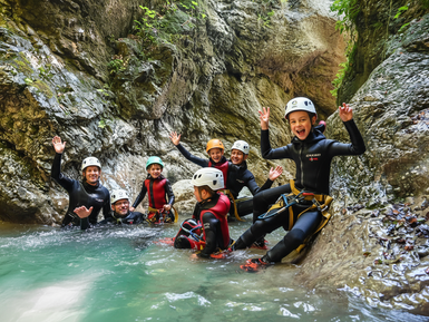 Eine Gruppe von sieben Personen in Neoprenanzügen genießt das Canyoning in einem klaren, grünen Wasserbecken.