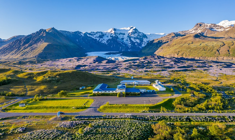 Eine weitläufige Landschaft mit einem Hotel im Vordergrund, umgeben von grünen Wiesen und majestätischen Bergen im Hintergrund.