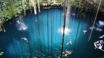 Personen schwimmen im klaren Wasser eines unterirdischen Cenote mit Lichtöffnung – Mexiko mit Kindern