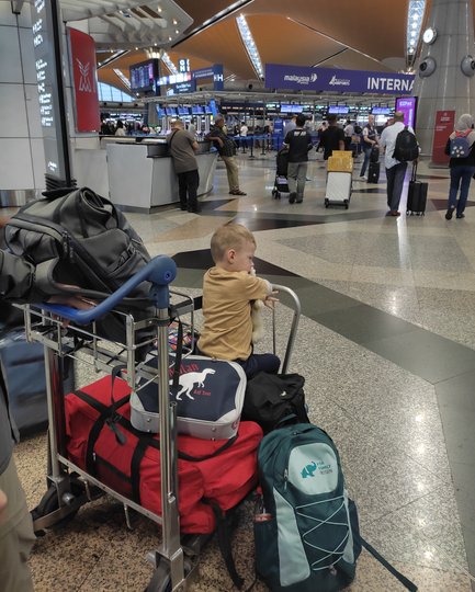 Baby sitzt auf dem Gepäckwagen bei der Anreise am Flughafen – Malaysia & Borneo Reise mit Kindern