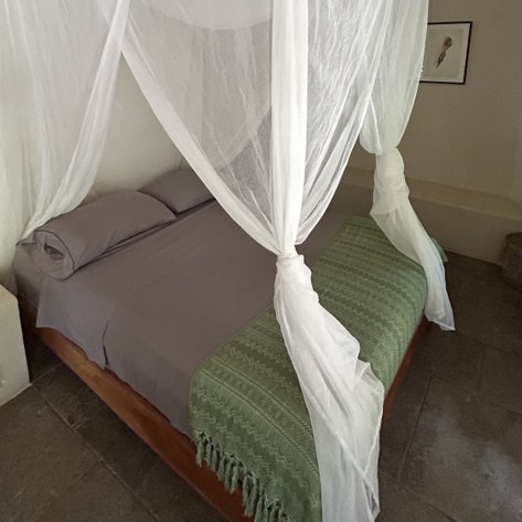 Ein gemütliches Schlafzimmer mit einem großen Bett, umgeben von einem weißen Moskitonetz und einer grünen Decke.