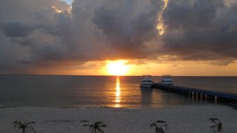 Ein atemberaubender Sonnenuntergang über dem ruhigen Meer, mit einem Steg, der zu zwei Booten führt.