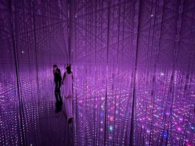 Zwei Personen stehen in einem Raum voller schimmernder Lichter, die in verschiedenen Farben leuchten und eine traumhafte Atmosphäre schaffen.