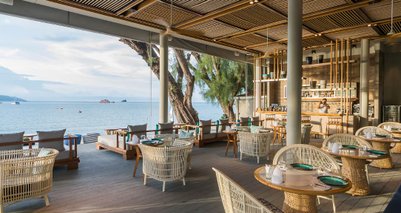 Ein elegantes Restaurant mit Blick auf das Meer, ausgestattet mit stilvollen Rattanmöbeln und einem einladenden Ambiente.