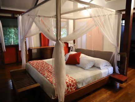 Ein gemütliches Schlafzimmer mit einem Himmelbett, umgeben von weißen Vorhängen und einem warmen Holzfußboden.