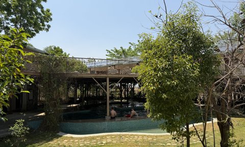 Ein ruhiger Außenbereich eines Camps mit einem Pool, umgeben von üppigem Grün und einem klaren blauen Himmel.