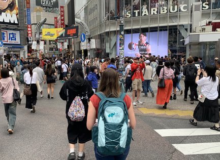 Eine belebte Straße in Shibuya, Tokio, mit vielen Fußgängern und einem großen Starbucks-Schild im Hintergrund.