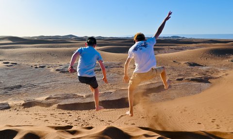 Kinder springen und haben Spaß auf den weiten Sanddünen der Sahara – Marokko Familienreise