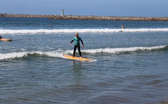 Ein junger Surfer balanciert auf einem orangefarbenen Brett und reitet eine Welle im klaren Wasser des Strandes.