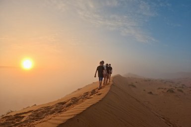 Familie wandert über eine hohe Sanddüne in der Wüste – Oman Familienreise