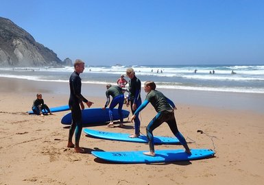 Eine Gruppe von Surfschülern übt auf blauen Surfbrettern am Strand, während die Wellen sanft an den Ufer schlagen.
