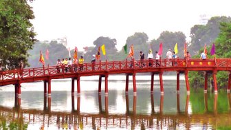 Eine Gruppe von Menschen überquert eine rote Holzbrücke, umgeben von grüner Natur und einem ruhigen See.