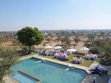 Ein Blick auf den Pool des Hotels Mandawa Haveli, umgeben von eleganten Tischen und Sonnenschirmen im Freien.