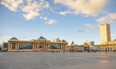 Der Sukhbaatar-Platz in Ulaanbaatar zeigt beeindruckende Architektur und eine lebhafte Menschenmenge unter einem blauen Himmel.