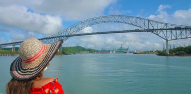 Eine Frau mit einem großen, bunten Hut blickt auf die beeindruckende Brücke über das Wasser in Panama-Stadt.