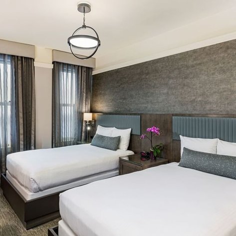Zwei Einzelbetten in einem modernen Hotelzimmer, umgeben von eleganten Vorhängen und stilvollem Mobiliar.