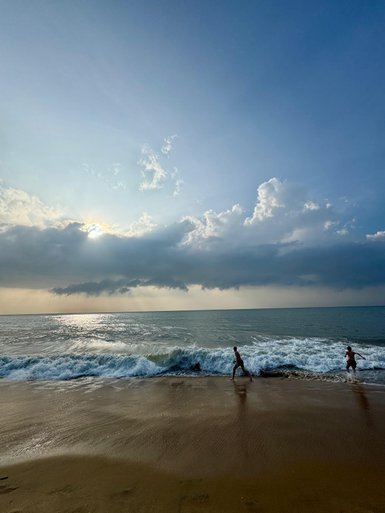 Zwei Kinder laufen am Strand entlang, während die Wellen sanft an den Ufer schlagen und der Himmel bewölkt ist.