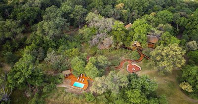 Eine Luftaufnahme eines rustikalen Camps, umgeben von üppigem Grün und Bäumen, mit einem kleinen Pool im Vordergrund.