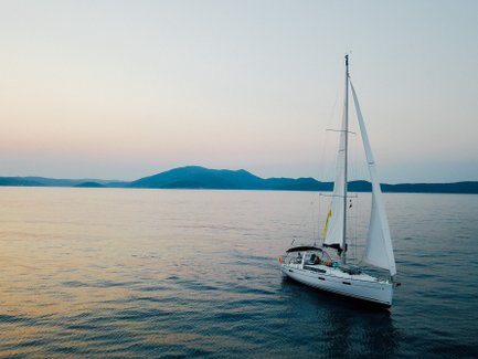 Ein Segelboot gleitet sanft über das ruhige Wasser, umgeben von sanften Hügeln im Hintergrund und einem zarten Abendhimmel.