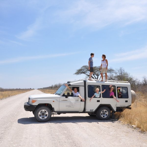 Eine Familie sitzen in einem Jeep. Zwei Personen stehen auf dem Dach des Jeeps - Namibia Familienurlaub