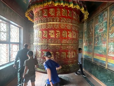 Eine Gruppe von Kindern und Erwachsenen dreht gemeinsam eine große Gebetsmühle in einem buddhistischen Tempel in Nepal.
