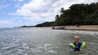 Kleines Kind planscht fröhlich im seichten Wasser am Strand – Costa Rica Reise mit Kindern