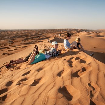 Kinder sitzen gemeinsam auf einer Wüstendüne – Oman Familienreise
