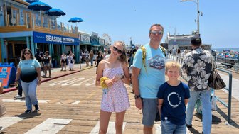 Eine Familie steht auf der Santa Monica Promenade, umgeben von Menschen und bunten Geschäften unter strahlendem Sonnenschein.