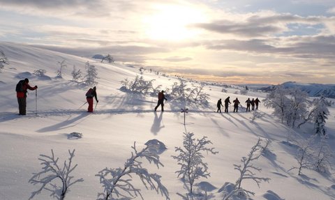 Eine Gruppe von Wanderern durchquert eine schneebedeckte Landschaft, während die Sonne hinter den Bergen untergeht.