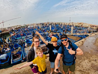 Familie macht Selfie vor blauen Fischerbooten im Hafen von Essaouira – Marokko Familienreise