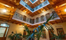 Ein einladender Innenhof mit Holzdecke und kunstvollen Geländern, umgeben von grünen Pflanzen und warmem Licht.