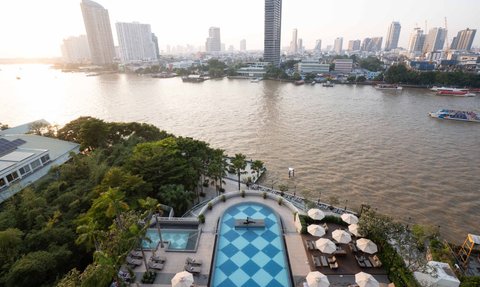 Ein Blick auf den Pool des Chatrium Hotels, umgeben von Palmen und Liegen, mit der Stadt Bangkok im Hintergrund.