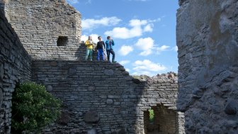 Kinder stehen in einer Burgruine und blicken Richtung Kamera
