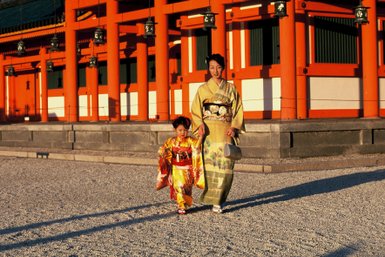 Eine Frau in einem eleganten Kimono und ein kleines Mädchen in einem bunten Kimono spazieren fröhlich im Heian-Schrein.