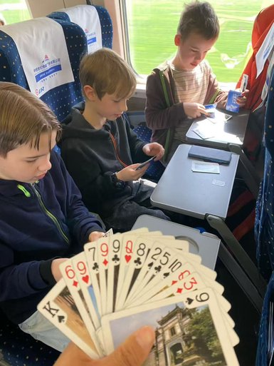 Drei Kinder sitzen im Zug und spielen Karten, während die Landschaft draußen vorbeizieht.