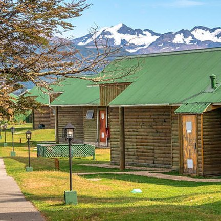 Holzhütten mit grünen Dächern stehen in einer malerischen Landschaft, umgeben von Bergen und klarem Himmel.