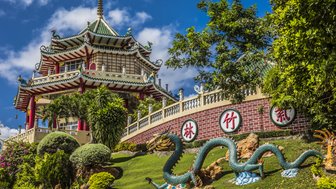 Ein prächtiger Tempel mit traditioneller Architektur erhebt sich über üppige Gärten und einen kunstvollen Drachen.
