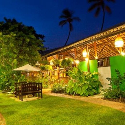 Der malerische Garten der Pousada Casa de Praia bei Nacht ist üppig mit Pflanzen und nostalgischem, sanftem Licht erleuchtet.
