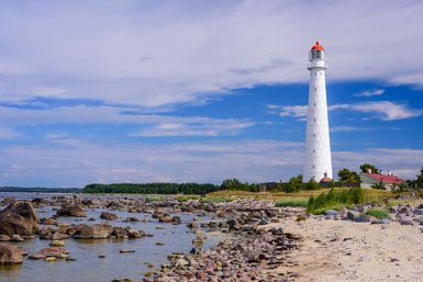 Ein hoher, weißer Leuchtturm mit rotem Dach steht majestätisch an der Küste, umgeben von glitzerndem Wasser und Felsen.