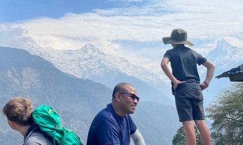Ein Junge mit einem Hut steht nachdenklich auf einem Felsen und blickt auf die majestätischen schneebedeckten Berge.