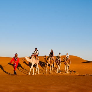 Familie zieht gemeinsam mit einer Kamelkarawane durch die Wüstenlandschaft der Sahara – Familienreise nach Marokko