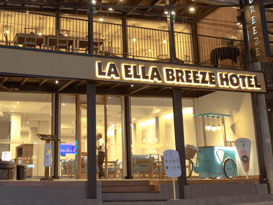 Die Fassade des La Ella Breeze Hotels zeigt eine einladende Atmosphäre mit warmem Licht und modernen Möbeln im Innenbereich.