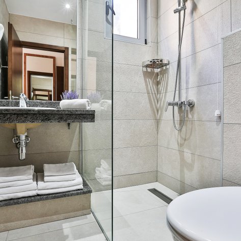 Ein modernes Badezimmer mit einer eleganten Dusche, einem Waschbecken aus Granit und frischen Handtüchern auf einem Regal.