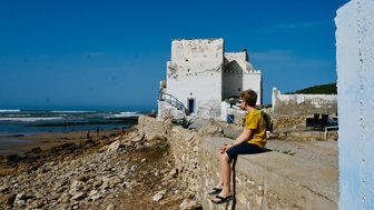 Kind genießt den Ausblick auf das Meer von einer Stadtmauer in Essaouira – Marokko Reise mit Kindern
