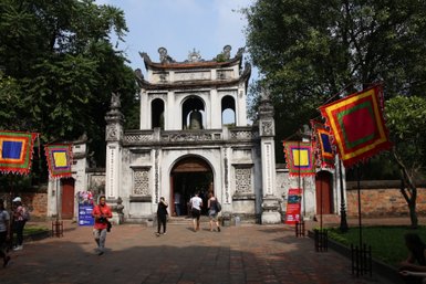Der Eingang zum Literaturtempel in Hanoi, umgeben von bunten Fahnen und Besuchern, die die historische Stätte erkunden.