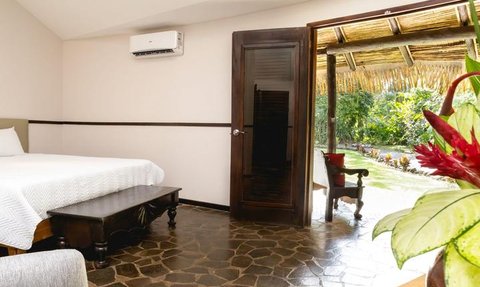 Ein einladendes Gästezimmer mit einem großen Bett, Holzdekor und Blick auf einen tropischen Garten durch eine offene Tür.